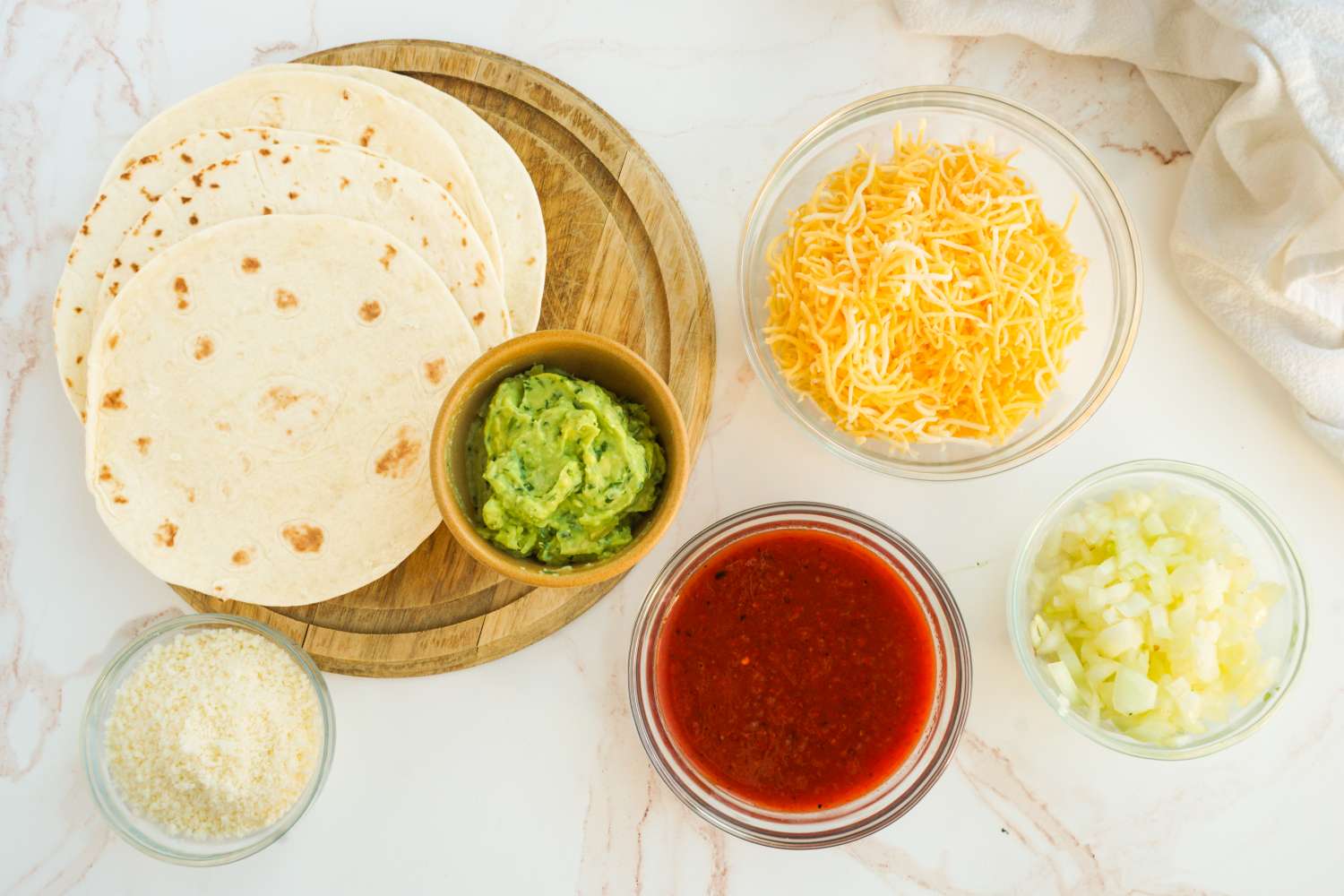 Ingredients including tortillas guacamole shredded cheese salsa and chopped onions arranged on a surface