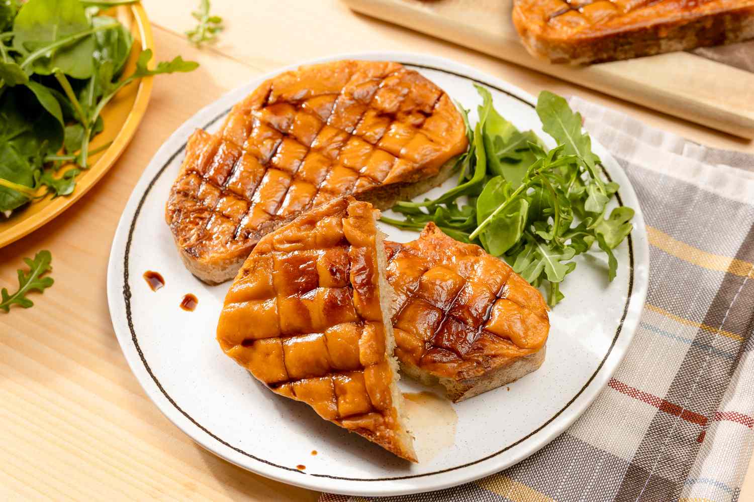 Serving of Welsh rarebit on plate with a side salad at a table with another serving on a plate and more welsh rarebit on a cutting board