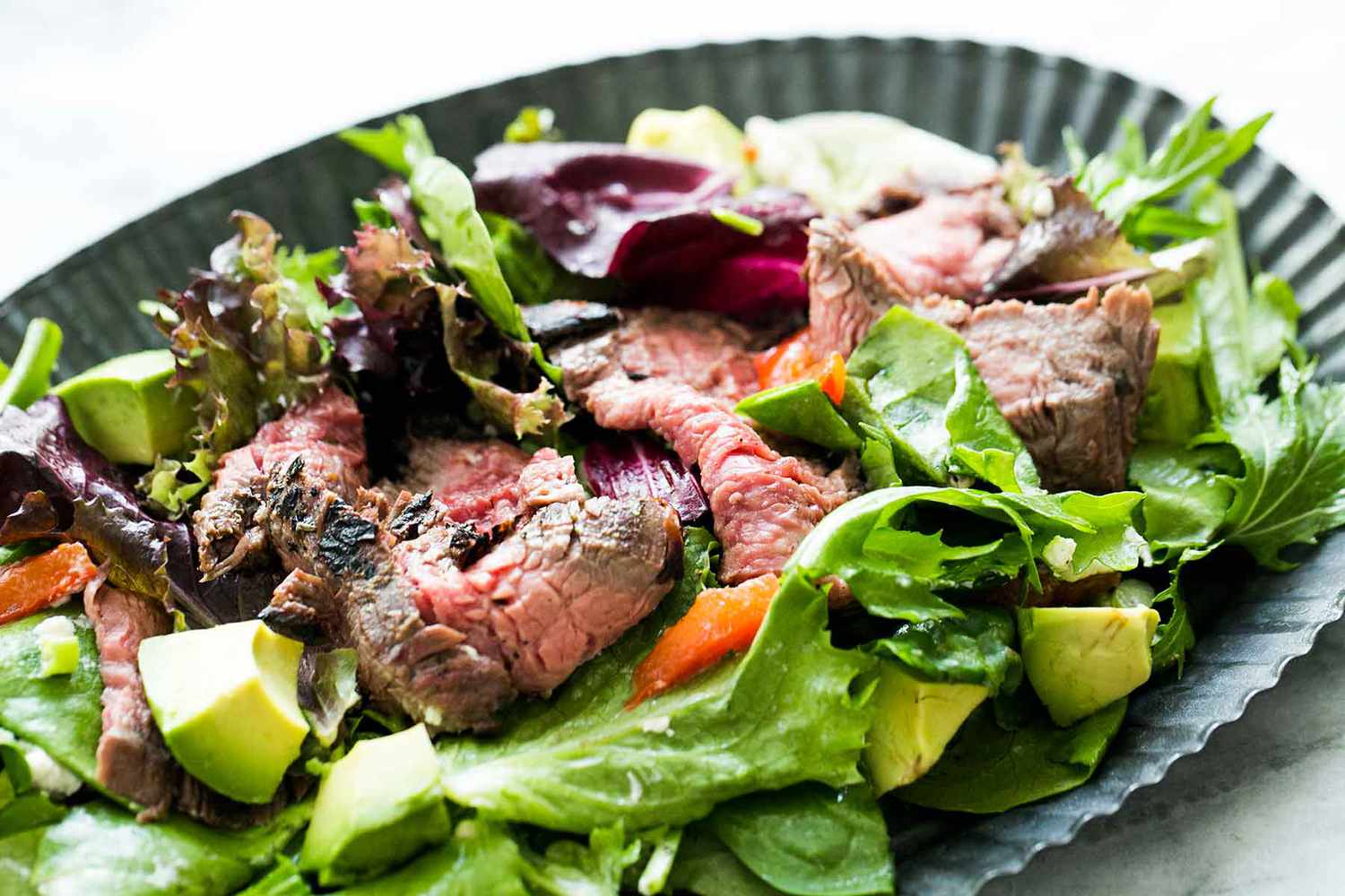 Steak salad made with thinly-sliced pan-seared flank steak on a bed of arugula and lettuce with avocado, pomegranate seeds, and other add-ins