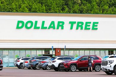 A parking lot in front of a Dollar Tree store with vehicles parked and a person standing by a car
