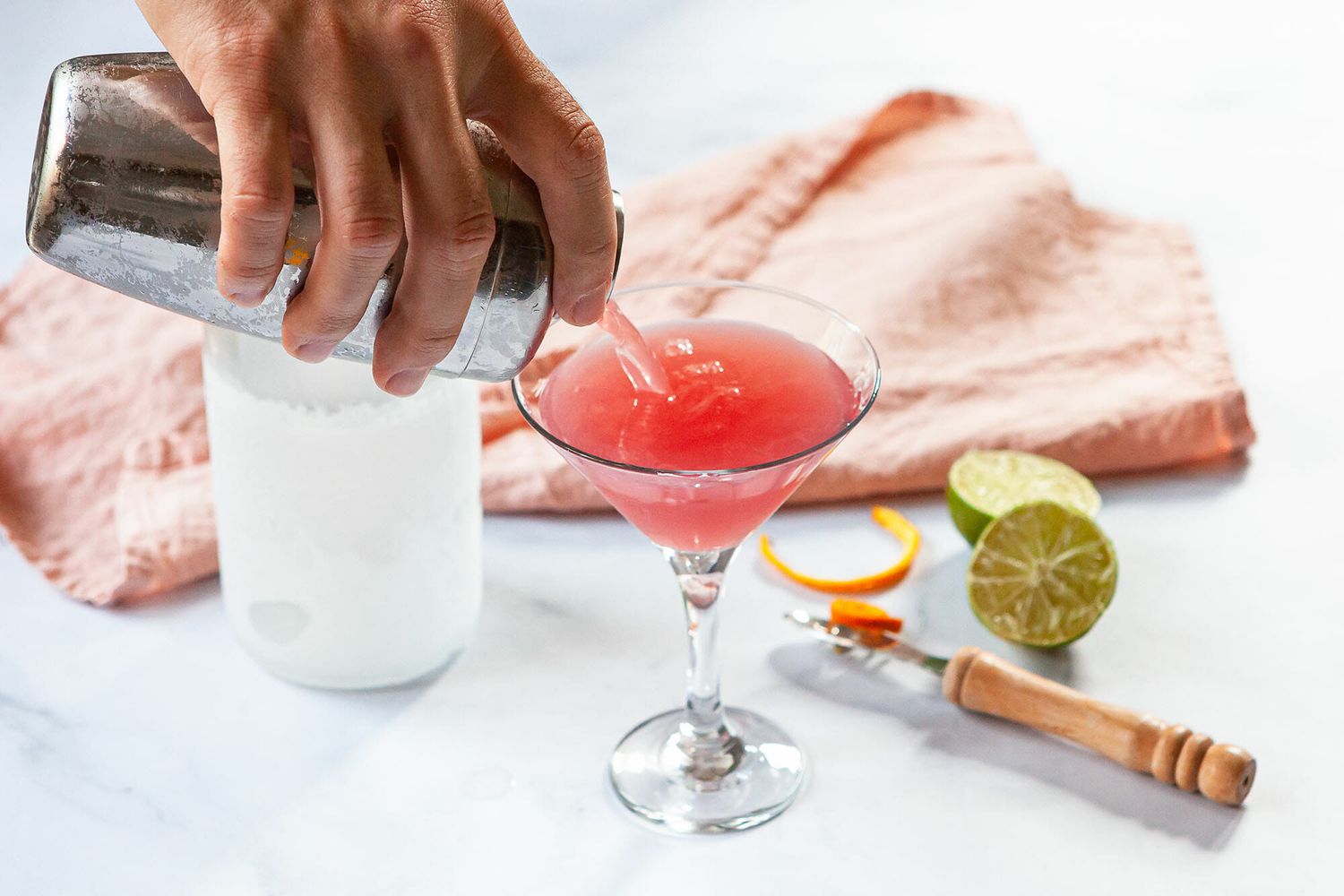 A cosmo recipe being made and poured into a martini glass.