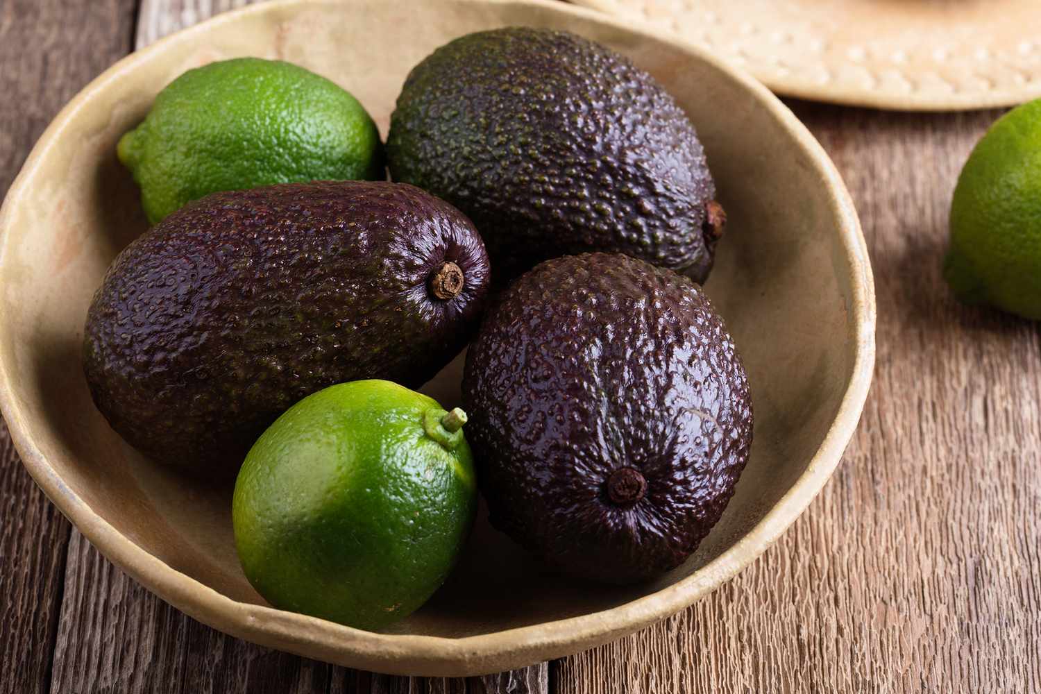 Bowl containing avocados and limes placed on a wooden surface