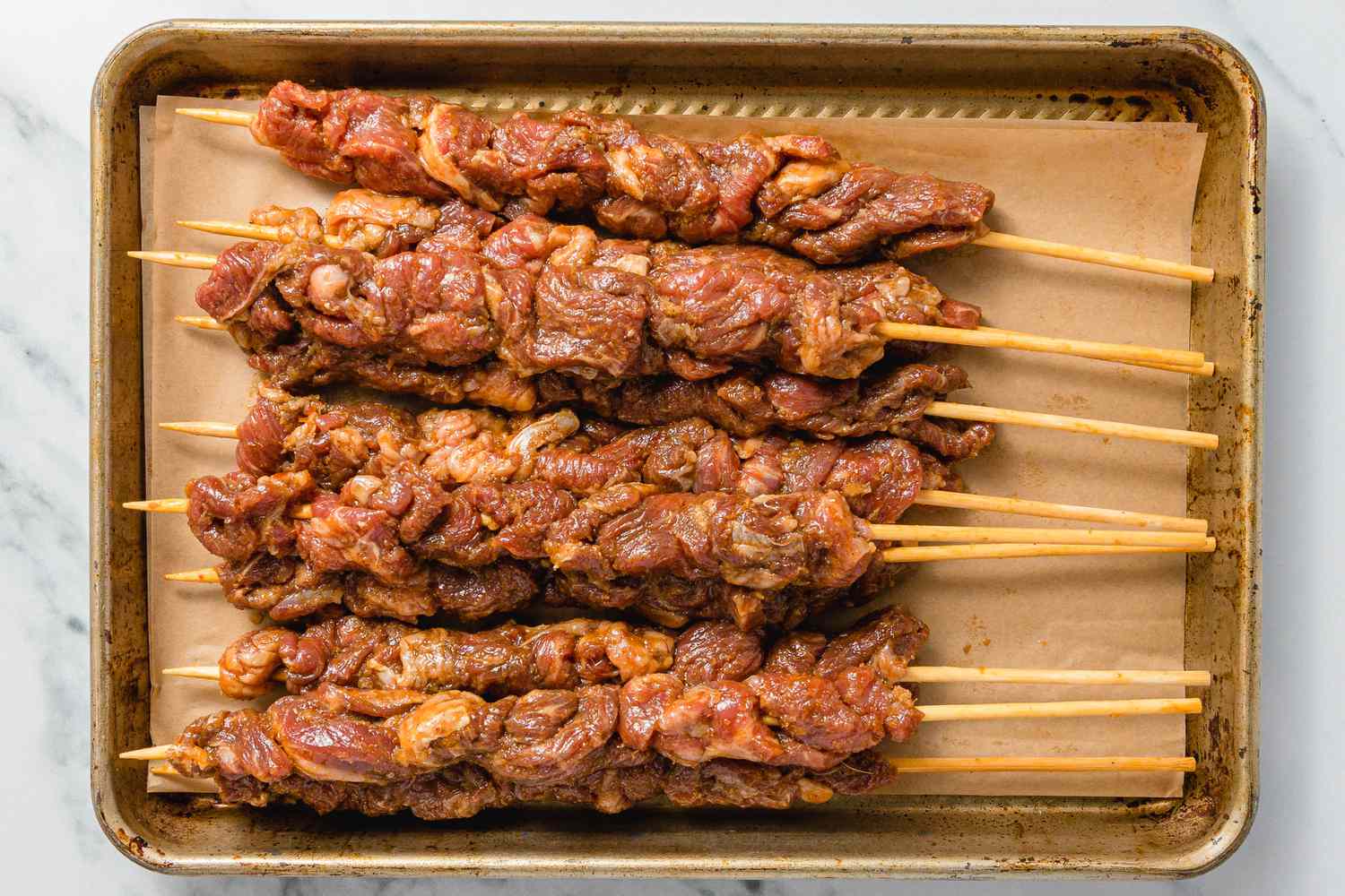Marinated Beef Added to Bamboo Skewers and Resting on a Parchment Paper Lined Baking Pan