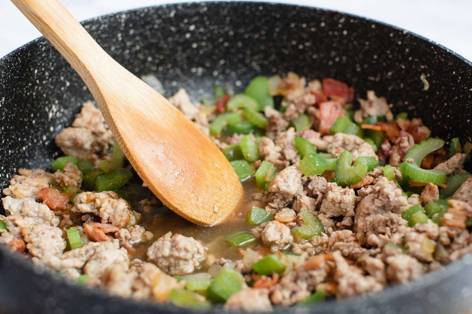 A wooden spoon mixes ingredients for a dirty rice recipe.