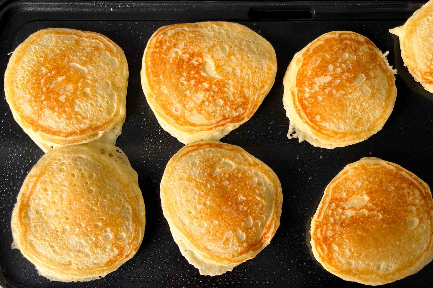 Several pancakes cooking on a griddle