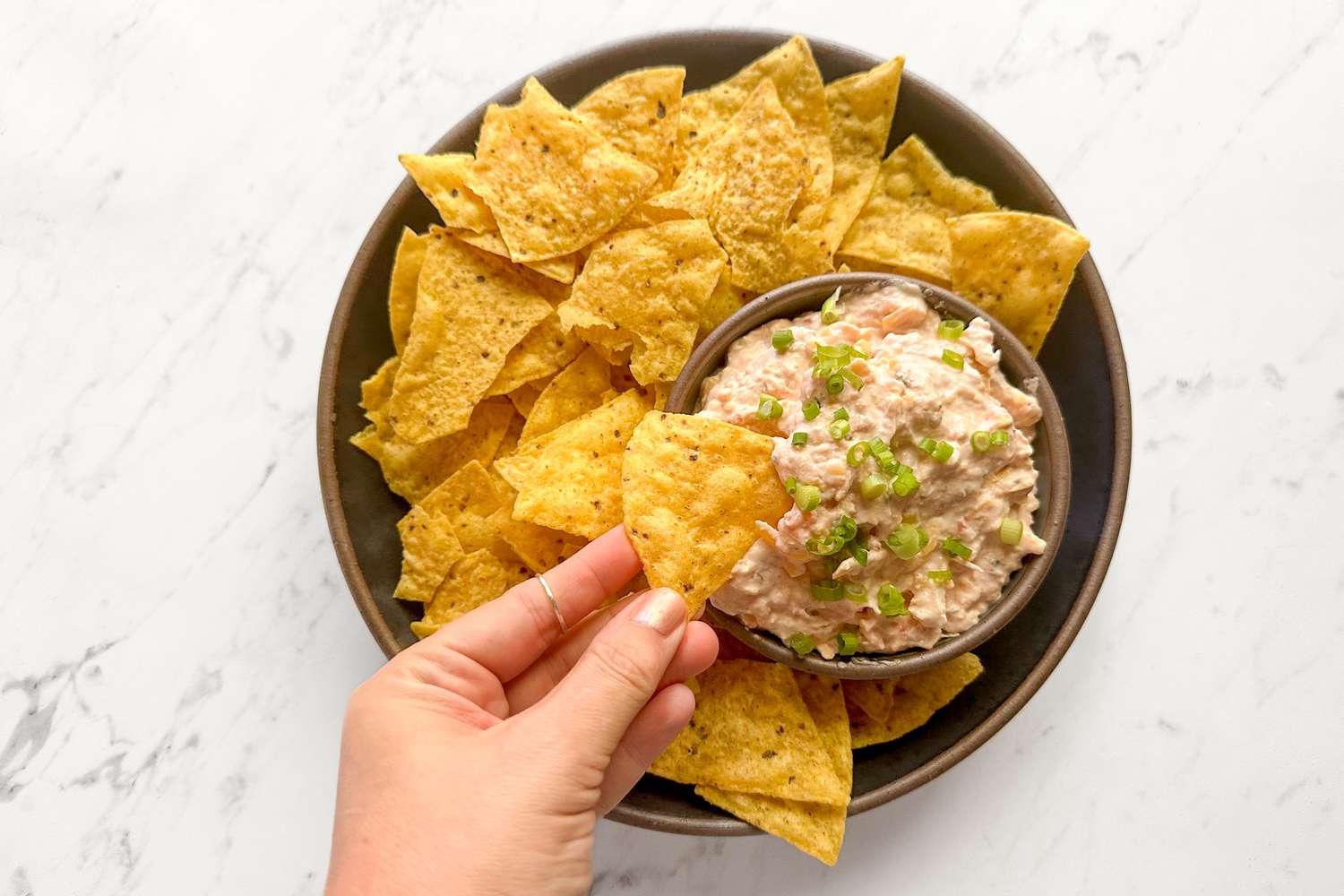 Bowl of tortilla chips and dip hand holding one chip
