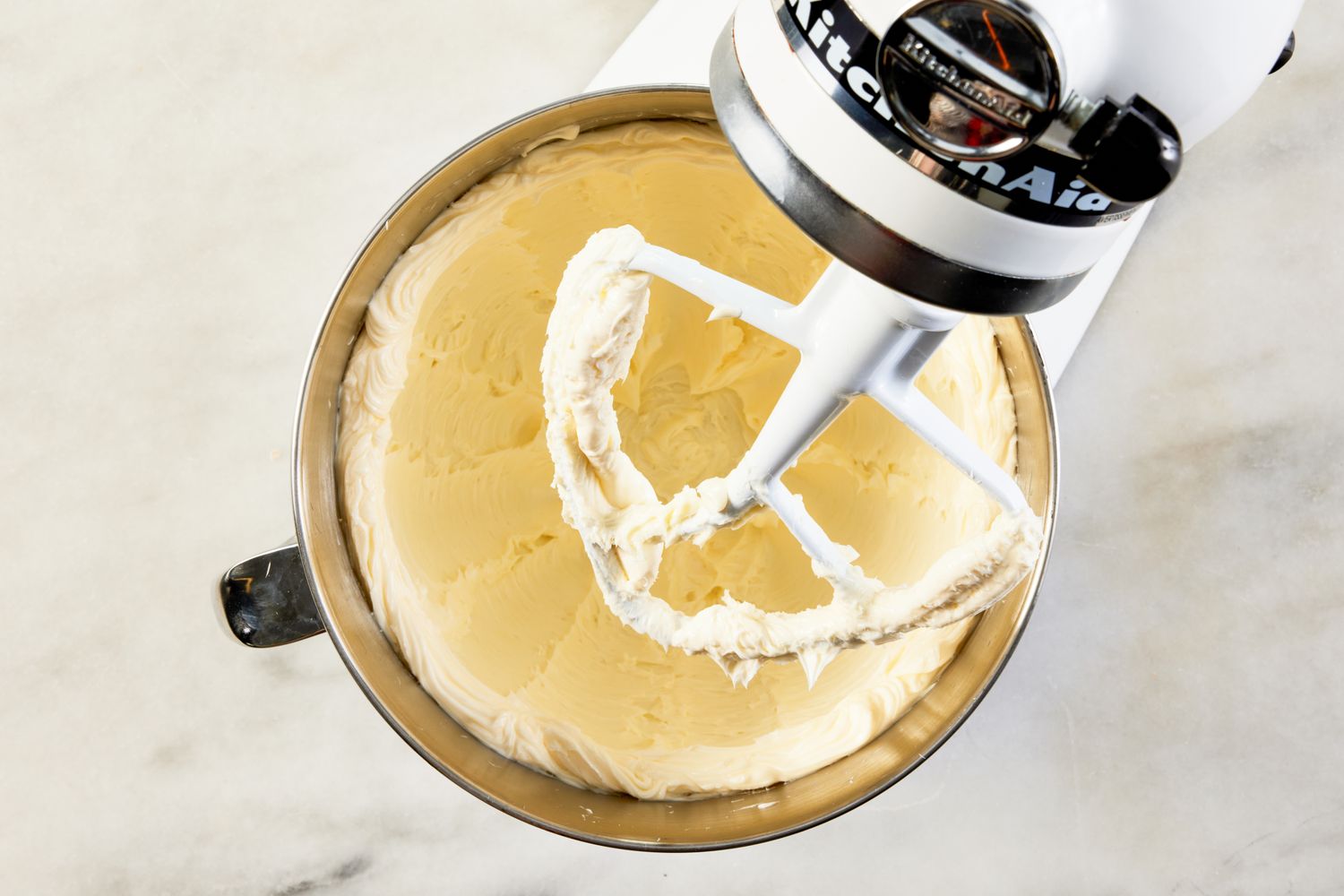 Stand mixer bowl filled with smooth whipped cream paddle attachment in view