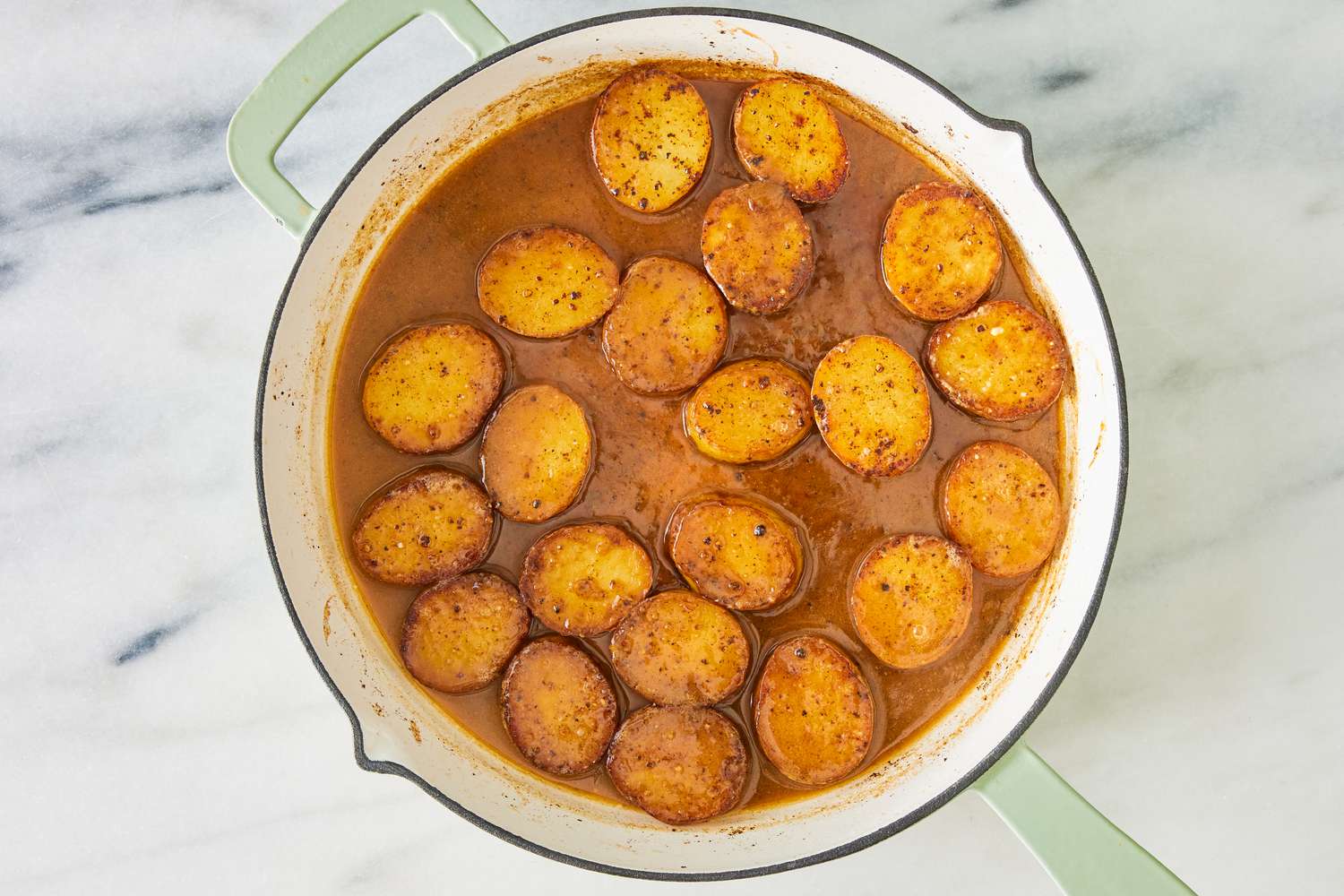 Roasted potato slices in a browned miso broth in a skillet for the miso melting potatoes recipe