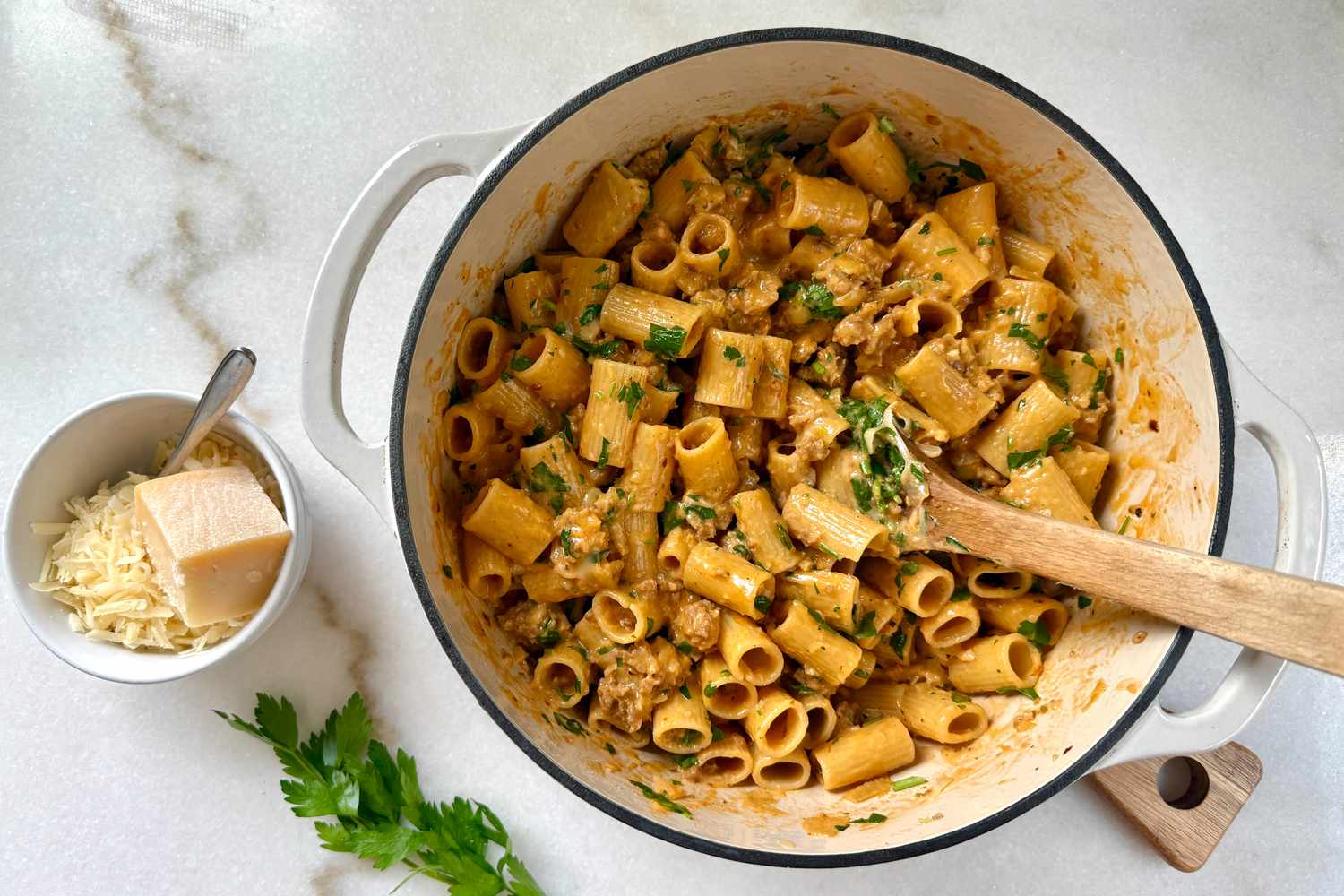 A pot of pasta with herbs placed next to grated cheese