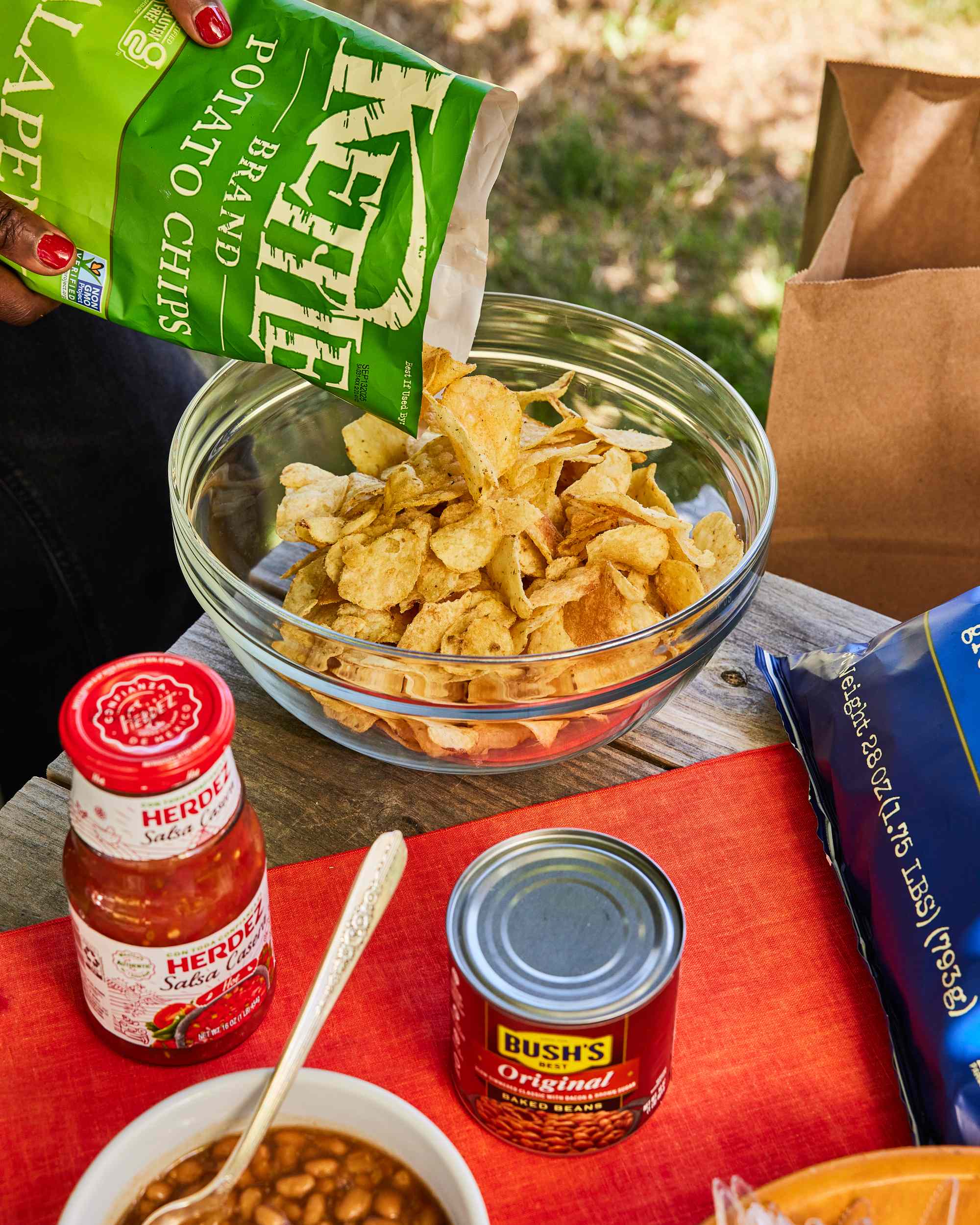 Pouring chips into a bowl, with jars and cans of food on the table