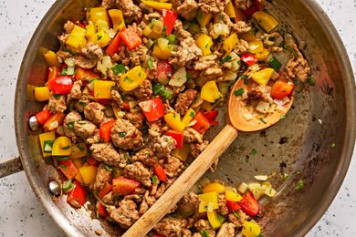 A skillet of cooked ground turkey and bell peppers with a wooden spoon in it