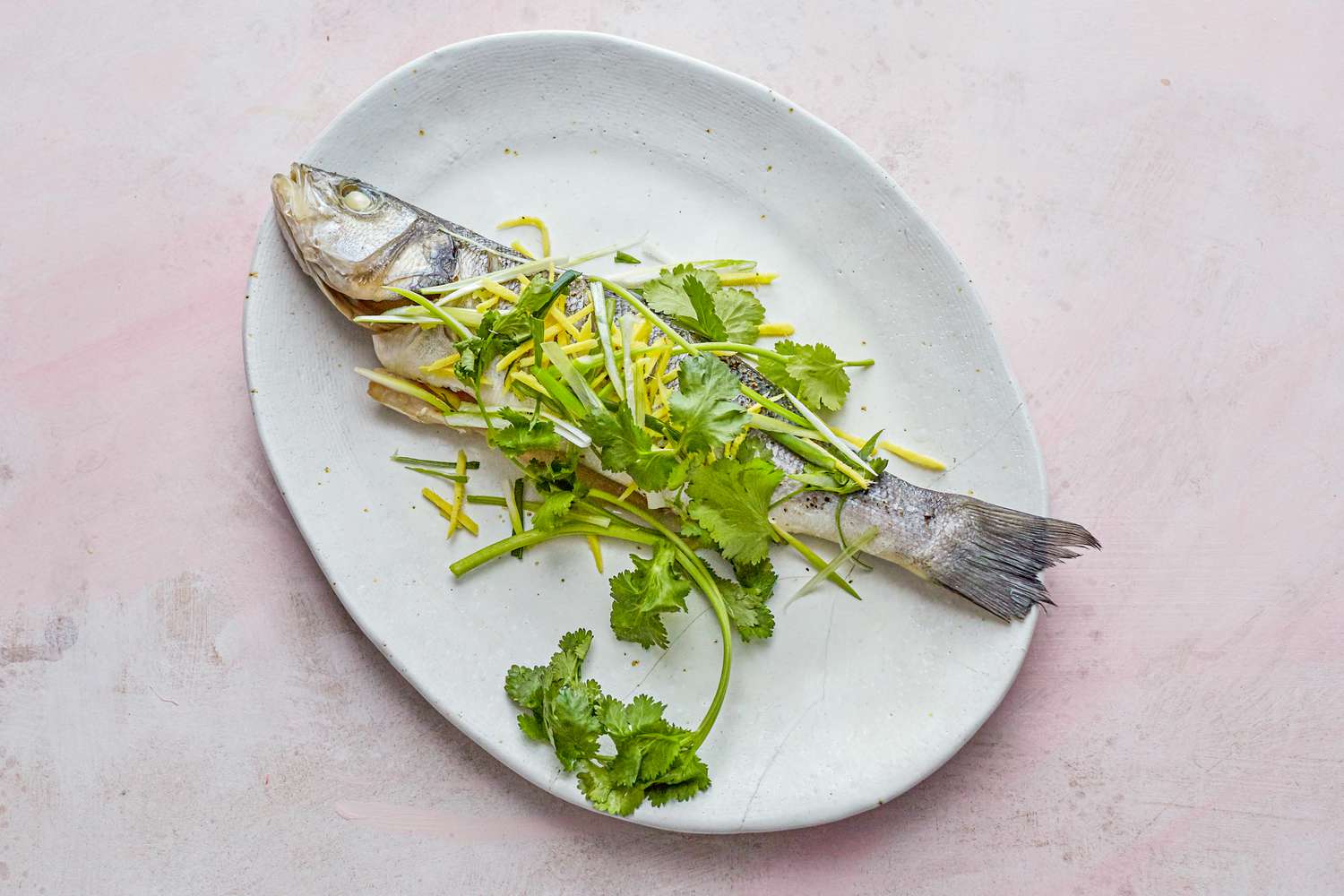 Whole steamed fish with ginger and scallions on a platter.