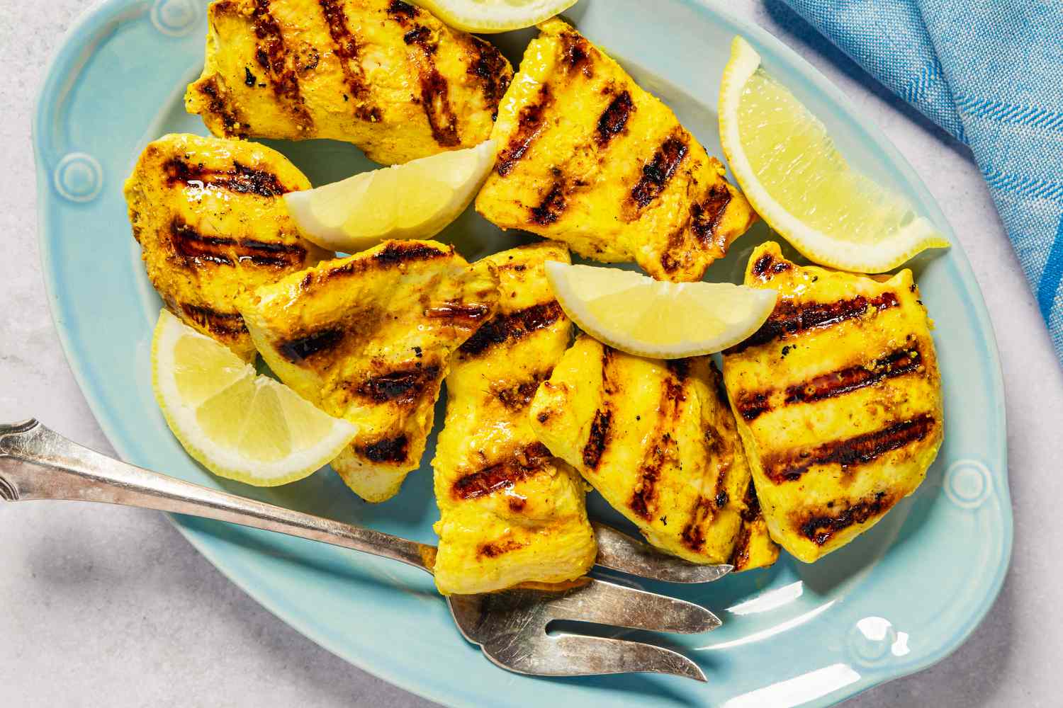 Grilled chicken pieces on a platter with lemon wedges and serving utensils