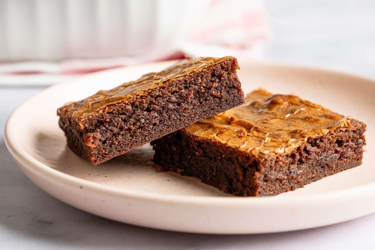 Closeup side view of two brownies on a small plate on a marble countertop with a blurred background