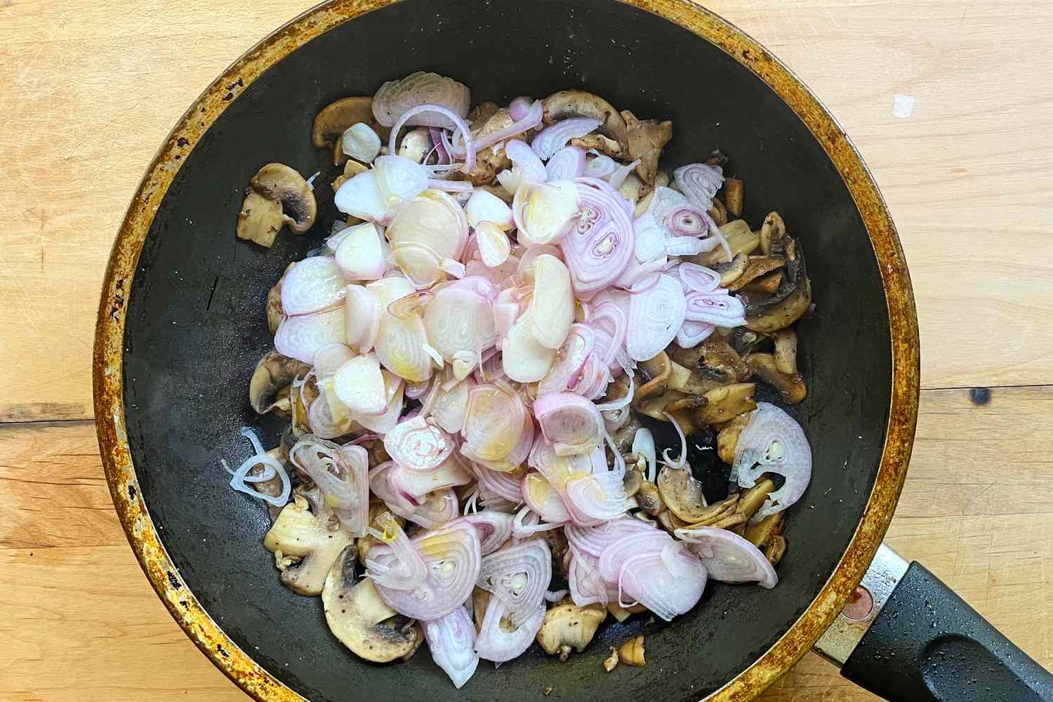 A skillet with sliced shallots and mushrooms being cooked