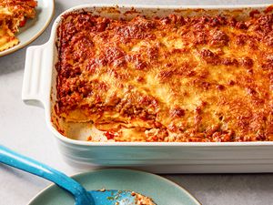 Side view of a white baking dish of Million Dollar Ravioli Casserole with a serving removed and on a small plate next to a serving spoon on a small plate
