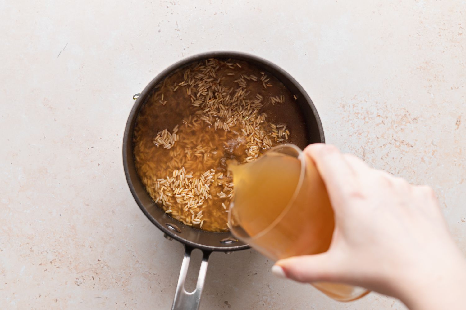Adding broth to rice in a bot for a vegetarian squash recipe.