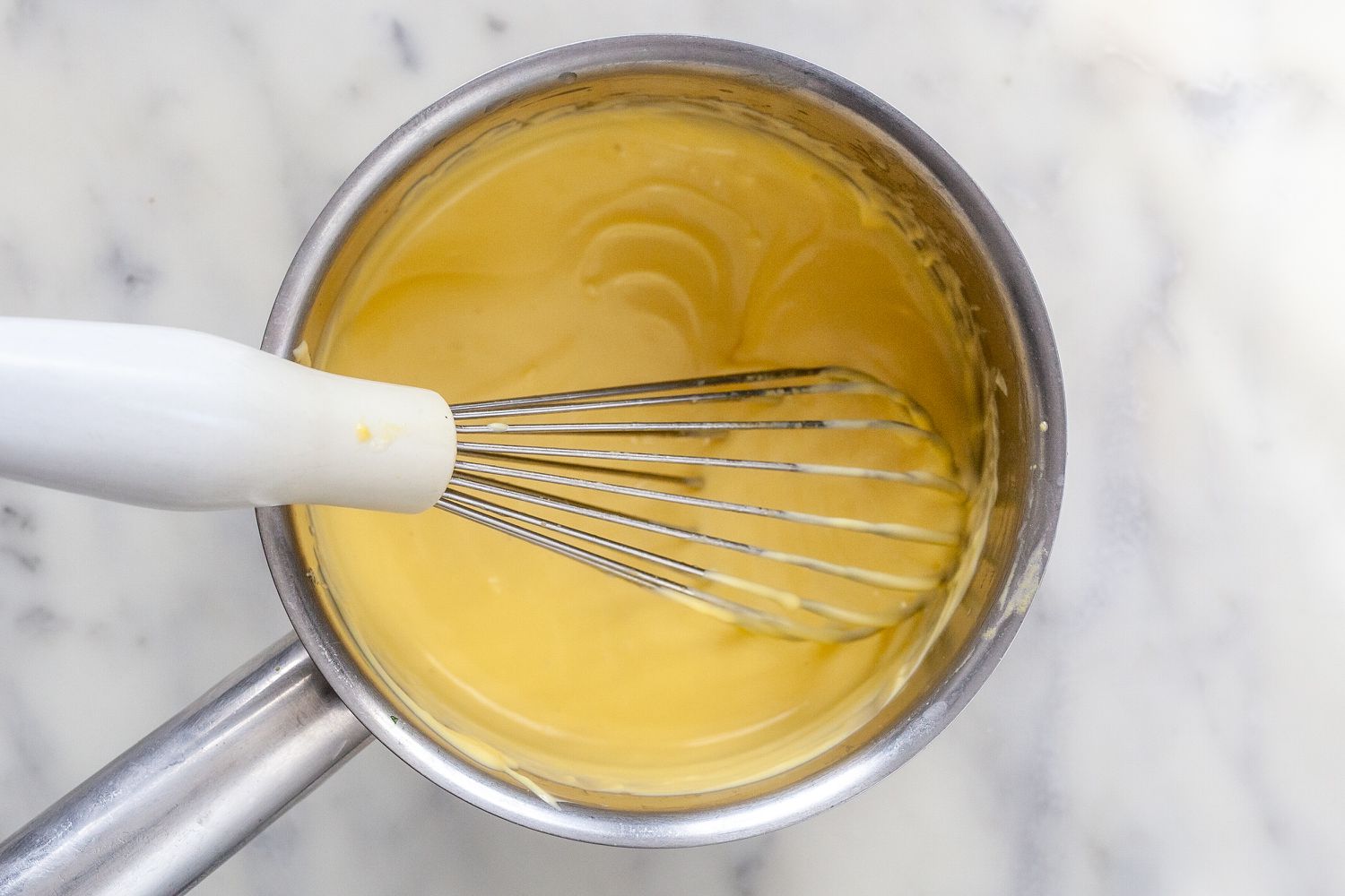 Whisking butter and egg yolk mixture in a saucepan to show how to make béarnaise sauce.