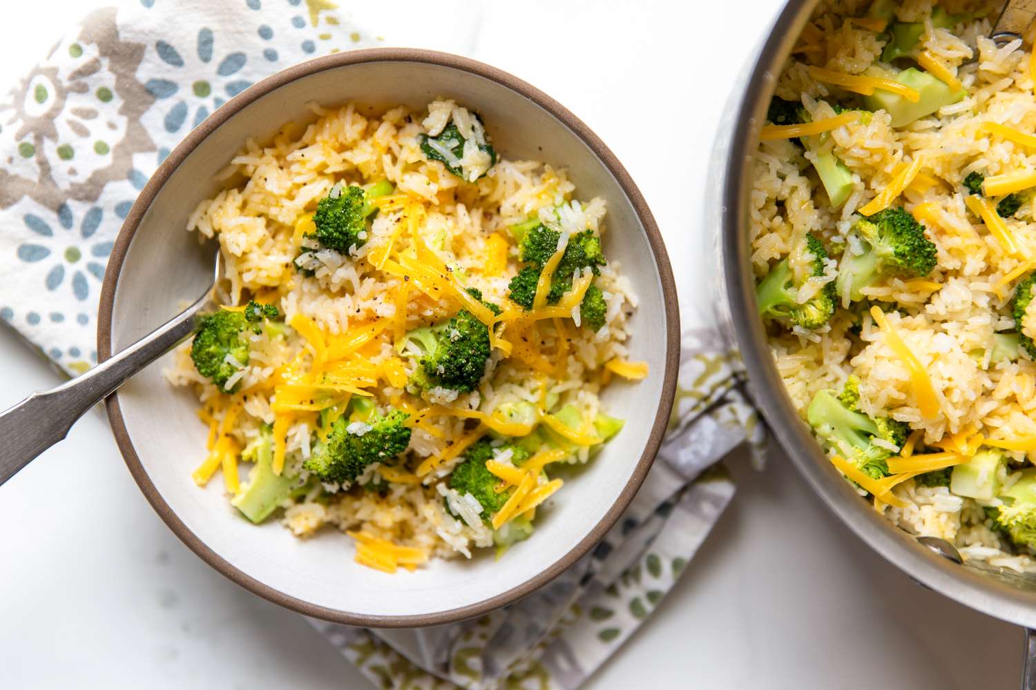 Cheesy broccoli rice served in a bowl beside a pot with the same dish accompanied by a floral napkin