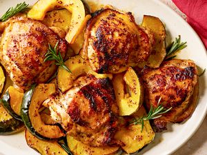 Overhead view of a white platter of maple glazed chicken and squash next to a red cloth napkin