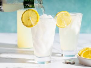 Glasses of lemonade with lemon slices ice and a pouring beverage