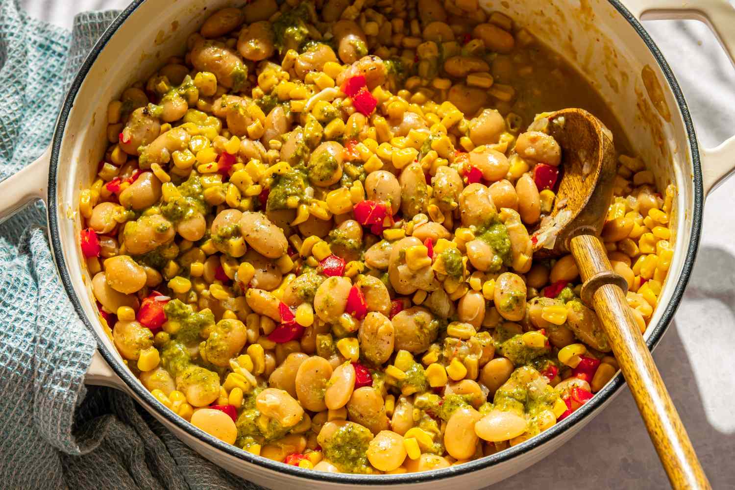 Pot of succotash with corn, lima beans, cherry tomatoes, seasoned sauce, wooden spoon on the side