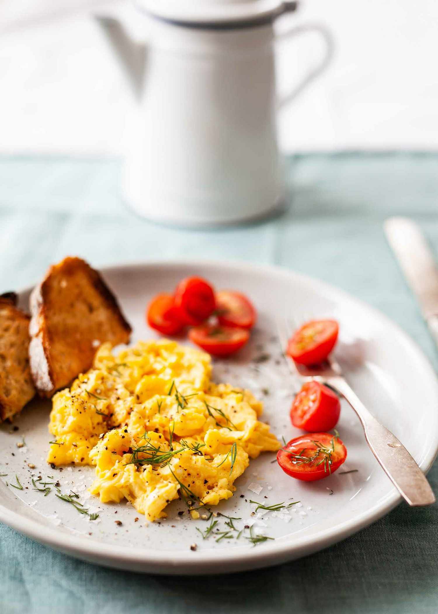 Scrambled eggs on a plate with tomatoes and toast off to the side