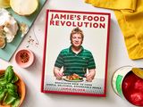 Jamie Olivers cookbook titled Jamies Food Revolution surrounded by cooking ingredients