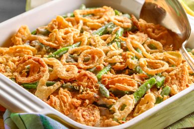 Closeup photo of a green baking dish of green bean casserole topped with fried onions along with a serving spoon