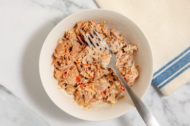 Tuna salad getting mixed together with a fork in a white bowl