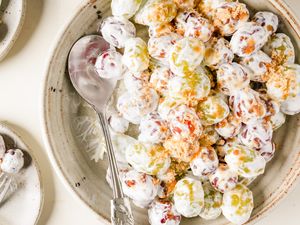 Bowl of grape salad with a spoon on the side topped with a creamy mixture and crumbled toppings