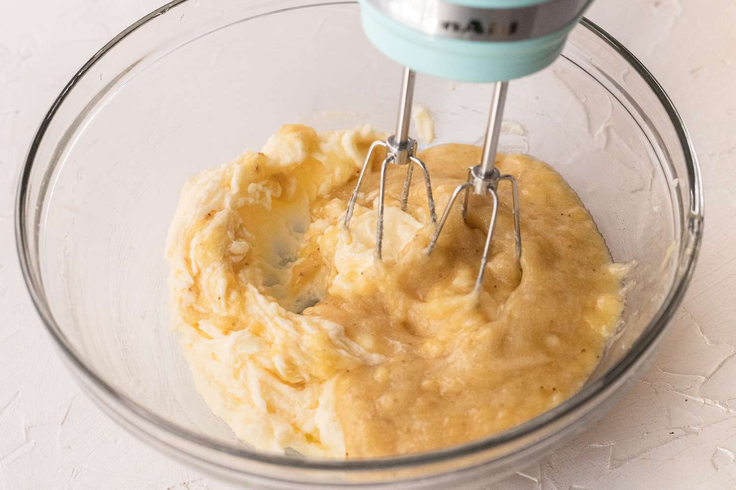 A hand mixer mixing the batter to make a banana cookie recipe.
