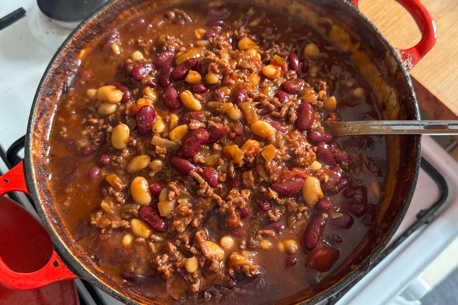 A pot of chili with beans and meat on a stove a ladle resting in the dish