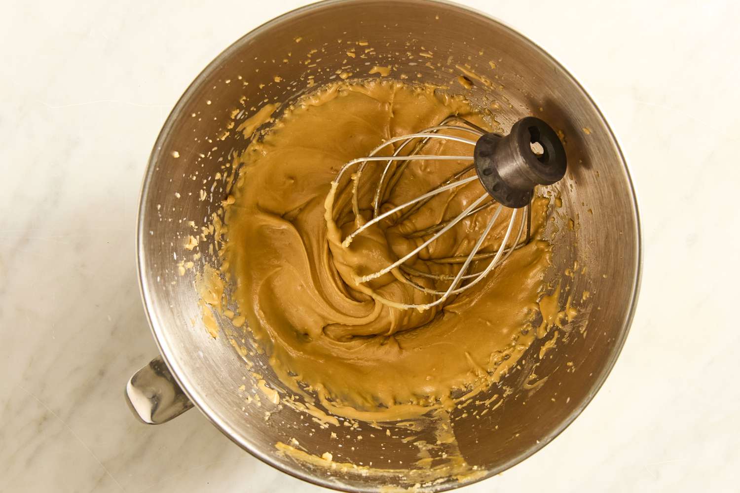 whipped caramel frosting in mixing bowl with a whisk mixer attachment for Grandma’s Oatmeal Cake
