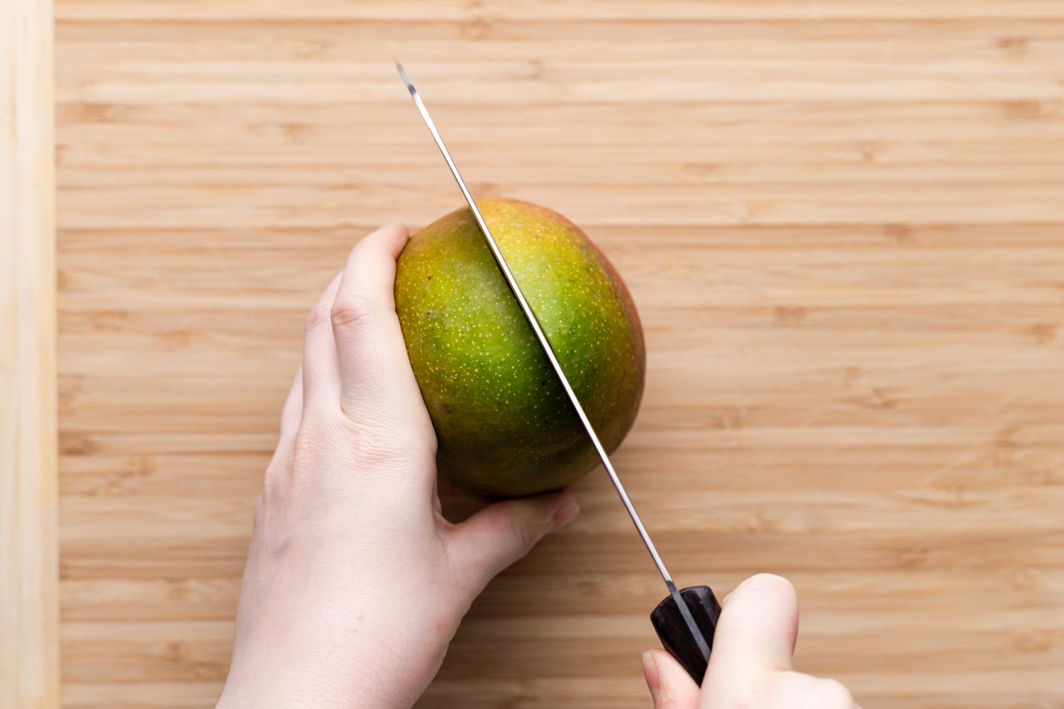 A person holding a knife and cutting into a mango to show how to cut a mango.