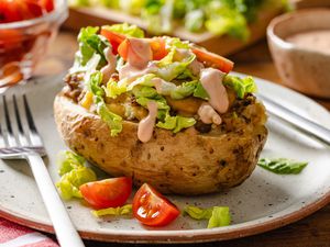cheeseburger stuffed baked potatoes on a plate at a table setting with bowls of toppings and sauce