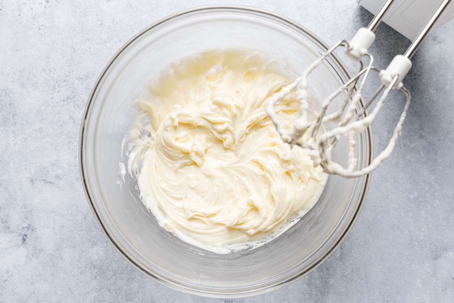 bowl with mixed icing, hand mixer beaters coated with icing positioned over the top of the bowl - Feather Cake