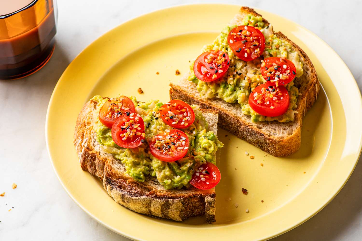 Two slices of avocado toast topped with cherry tomato halves and seasonings on a yellow plate