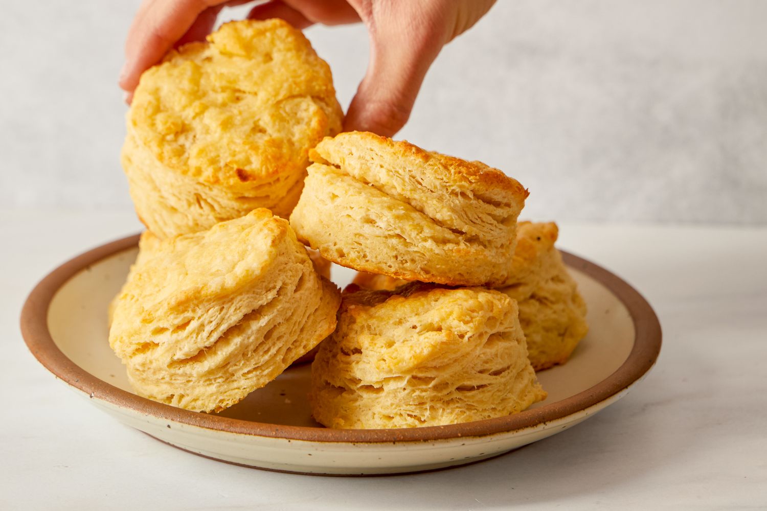A hand reaching for a biscuit from a plate containing multiple biscuits