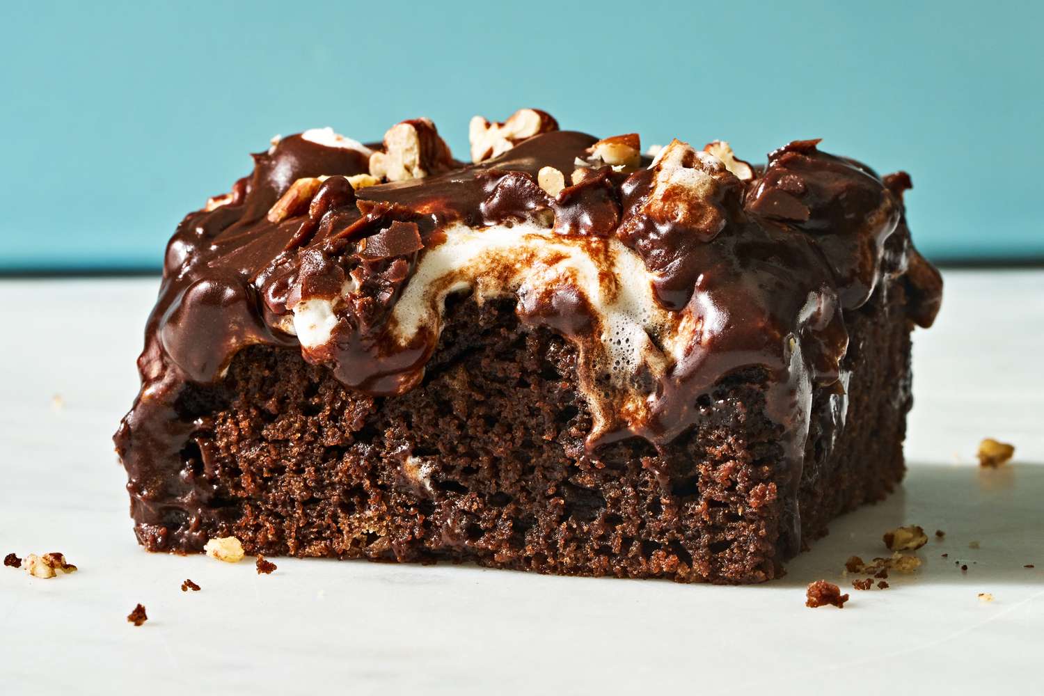 Closeup side view of a slice of Mississippi Mud Cake on a white surface and light blue background