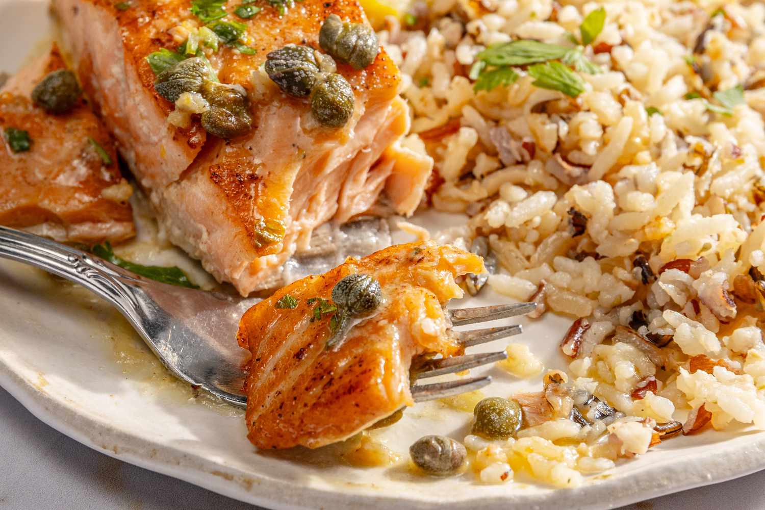 close up of Salmon Piccata with a bite ready on a fork and wild rice on the side