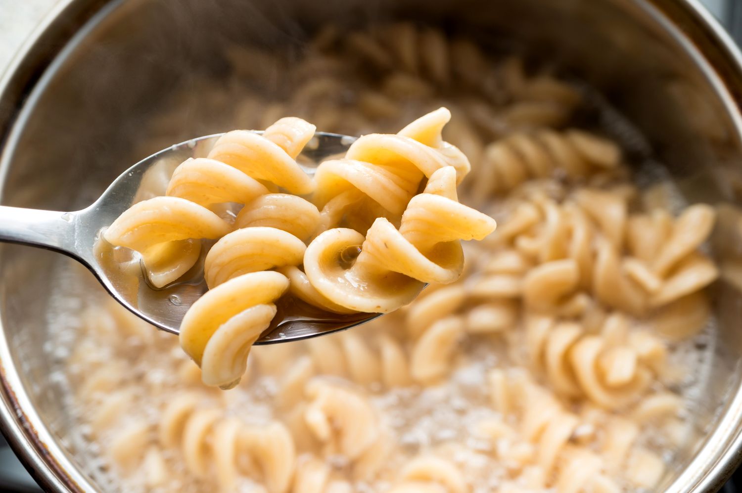 Cooked pasta being held up in a spoon over a pot of boiling water