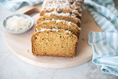 Slices of Zucchini Carrot Bread on Round Wood Board Next to Small Bowl of Coconut Flakes