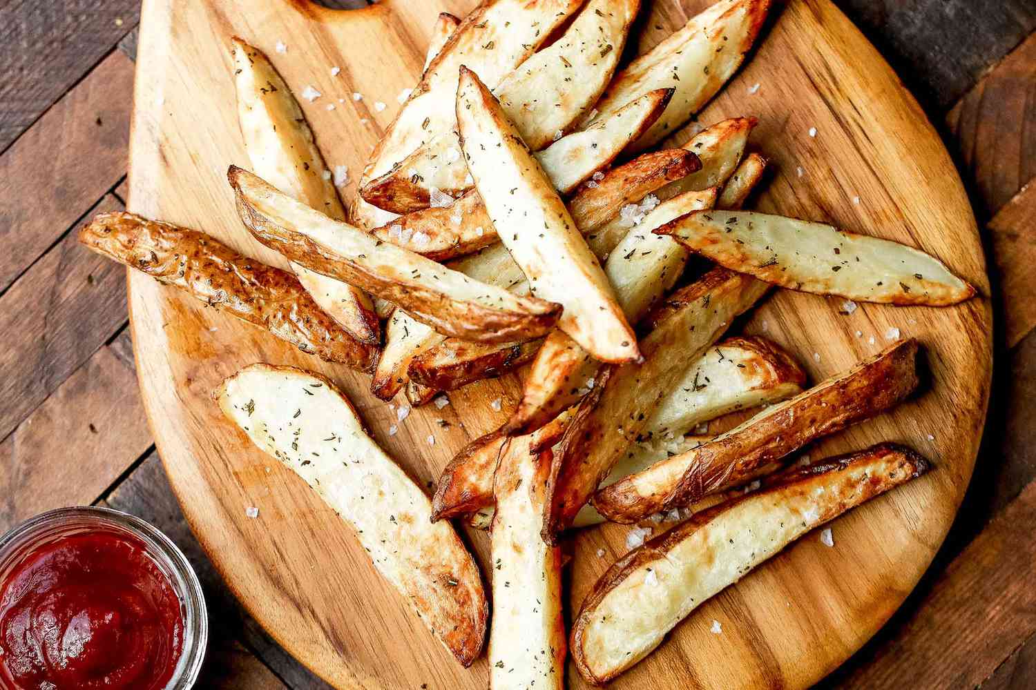 French fries served on a wooden platter alongside a small dish of ketchup