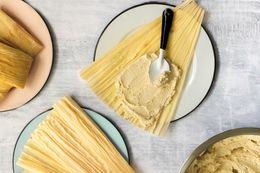 Bowl of Masa (Tamales Dough) Next to a Plate with a Corn Husk Smeared with Masa Using the Back of the Spoon and a Plate with More Corn Husks