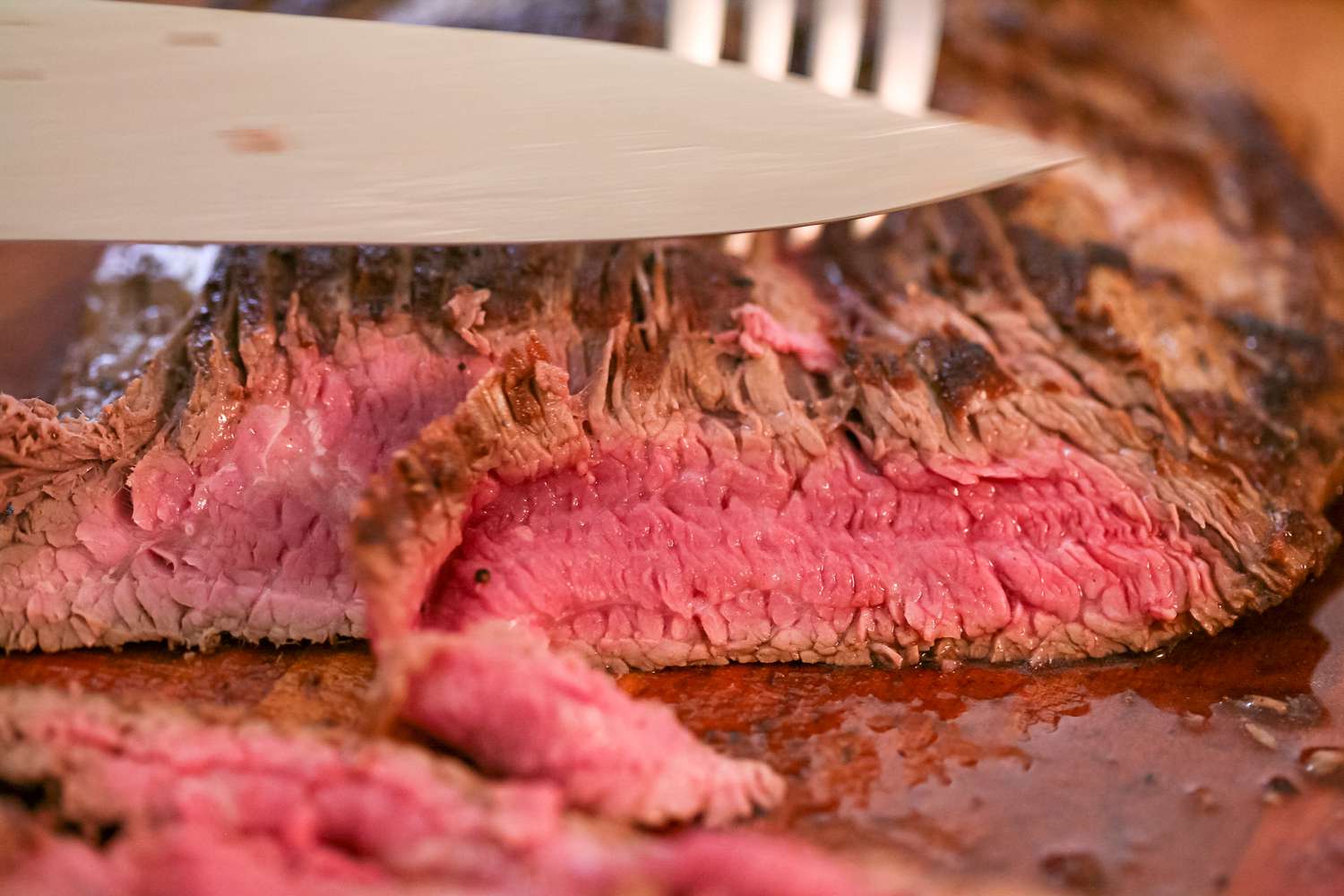 Slicing flank steak on a cutting board.