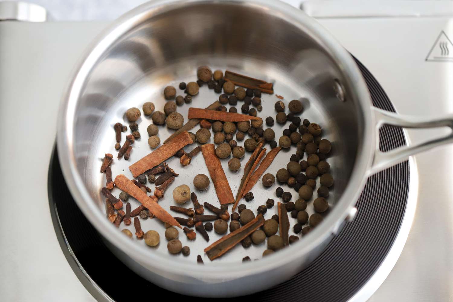 Cinnamon Sticks, Whole Allspice, Whole Black Pepper, and Cloves Toasting in a Pot Over an Induction Stove