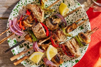 Grilled tuna kebabs with vegetables and lemon slices on a speckled plate