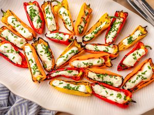 A serving platter of grilled mini peppers stuffed with feta cheese and garnished with chopped herbs