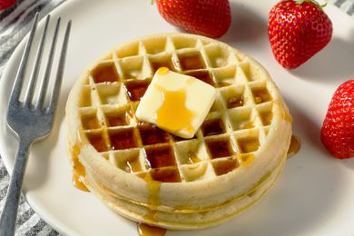 round waffles stacked on a plate with butter, syrup, and fruit